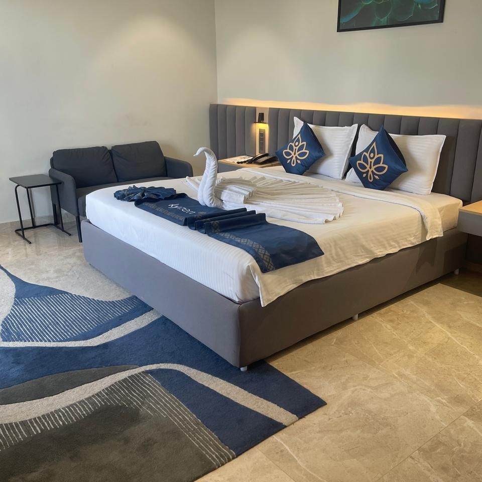 Well lit bedroom at Hotel Kyzen HiTech City with a king bed, blue carpet and a sitting area.